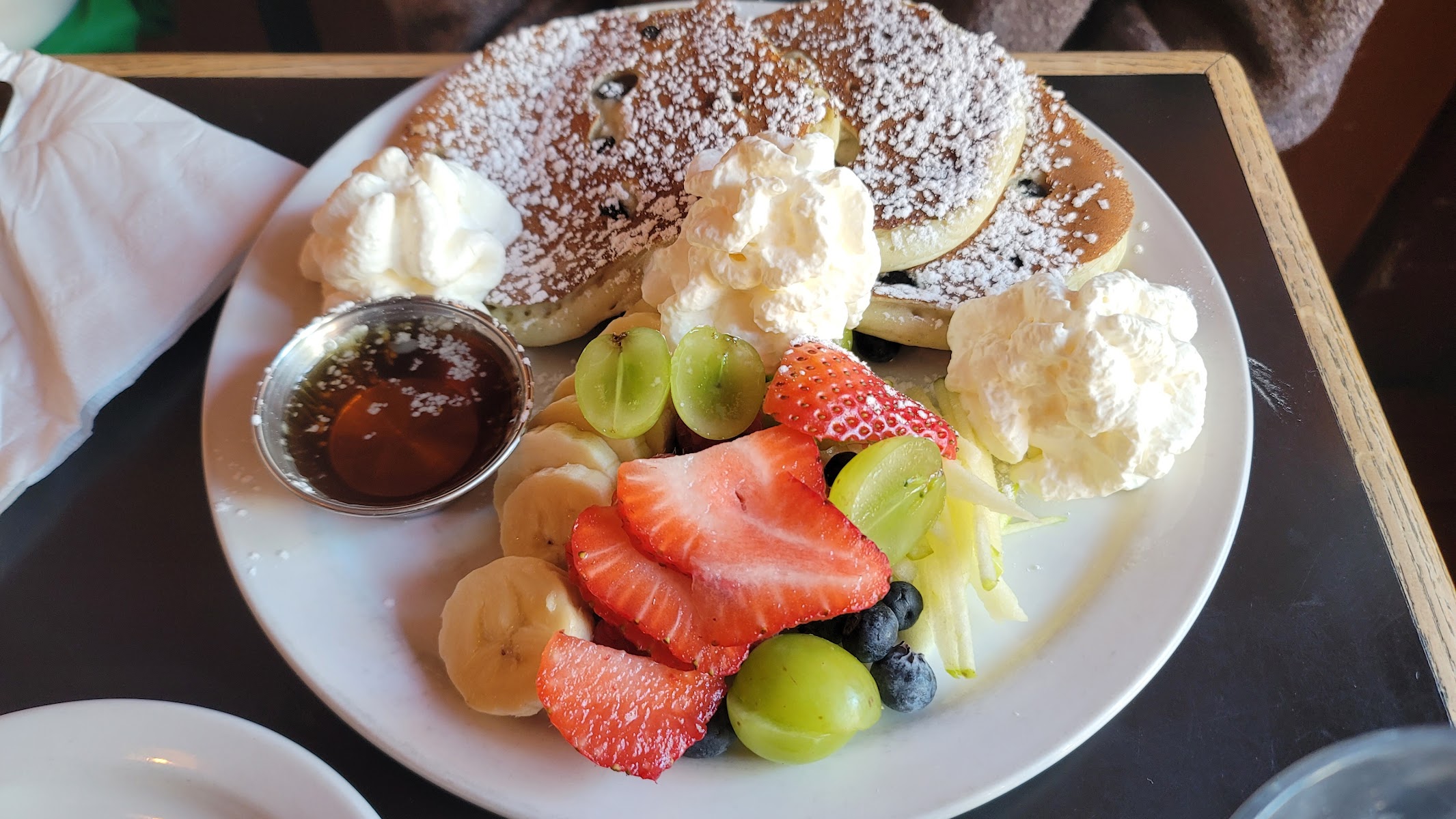 Pancakes topped with fresh fruit, whipped cream, and syrup at Petit Dejeuner