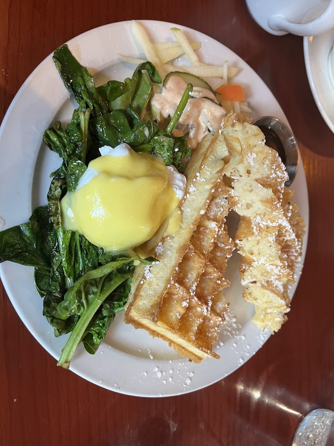 Poached egg over greens with waffles and bacon
